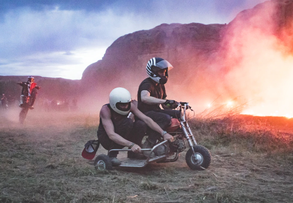 Two men racing a motorized tricycle around a bonfire